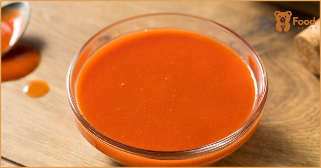 An artistic still life of buffalo sauce ingredients like red chili peppers, paprika, garlic, and vinegar, arranged on a vintage scale against a stone wall backdrop.