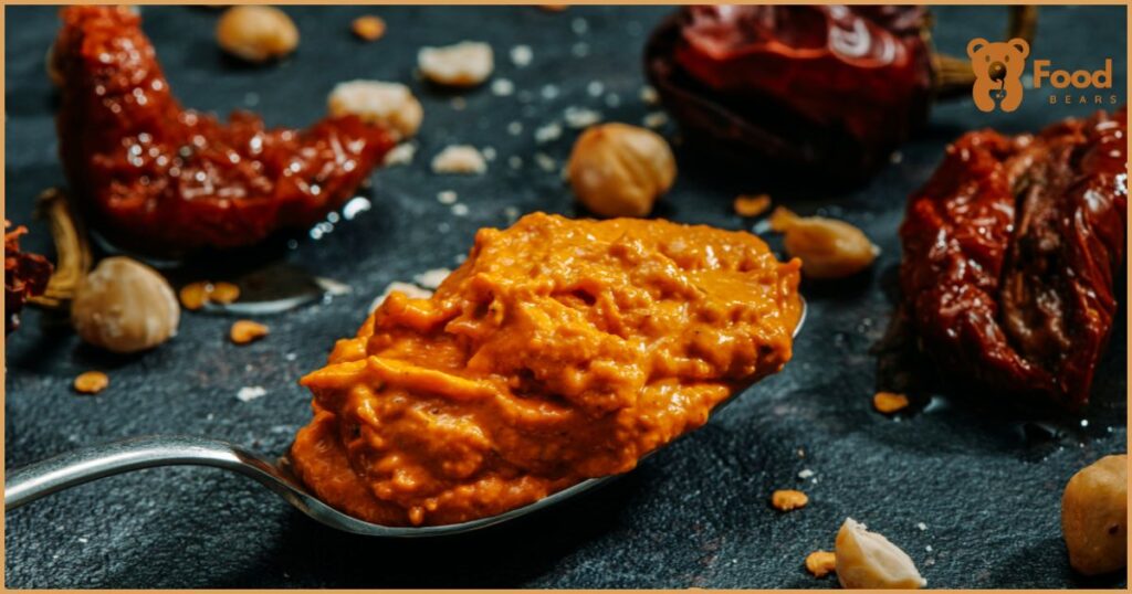 A vibrant kitchen scene with ingredients for romesco sauce displayed on a wooden cutting board, including a food processor with the partly blended sauce.